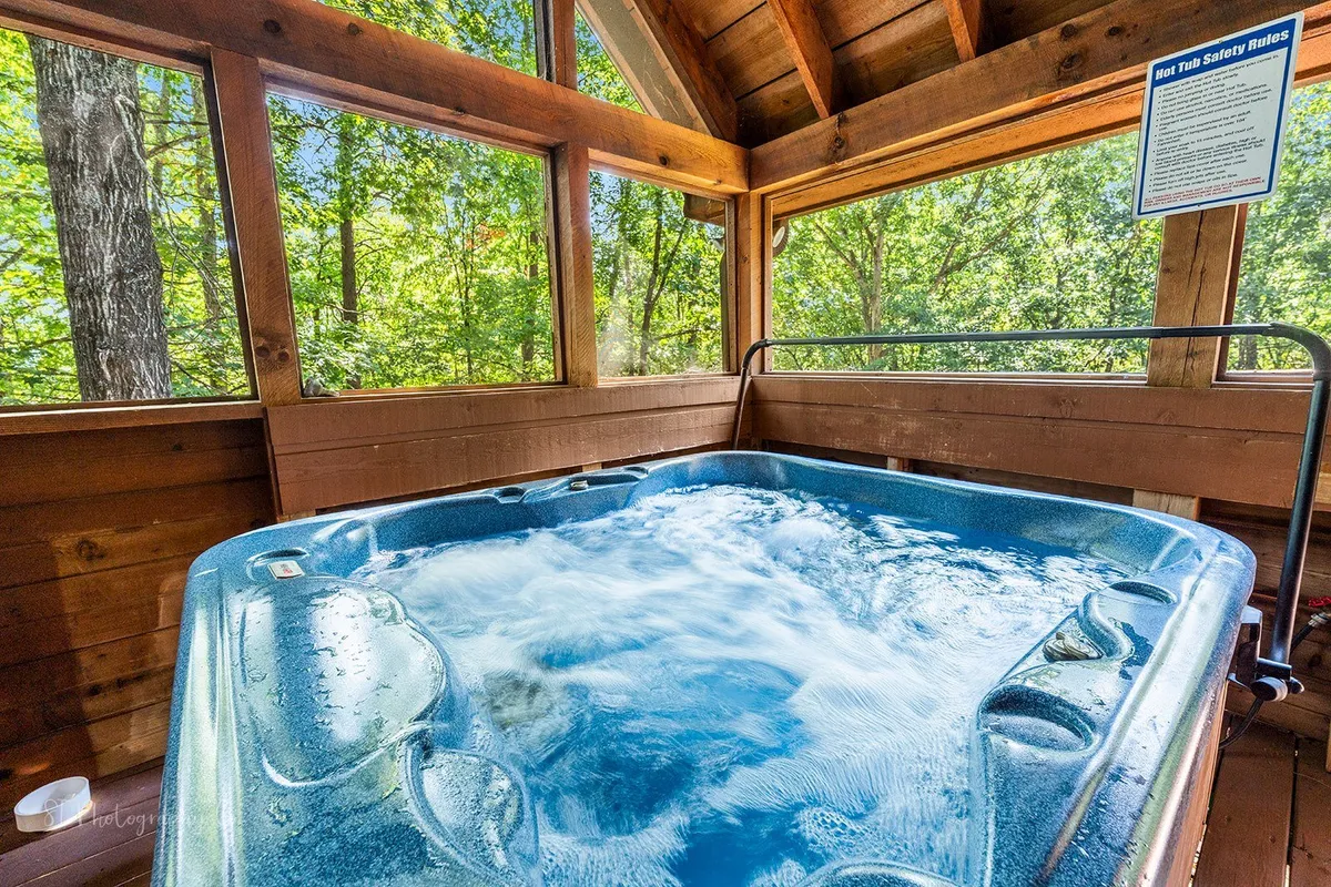 An indoor hot tub is set by large windows overlooking a wooded landscape, framed by warm wooden walls. The scene invites relaxation while being visually connected to the natural outdoors, perfect for a tranquil soak after a day of mountain adventures.