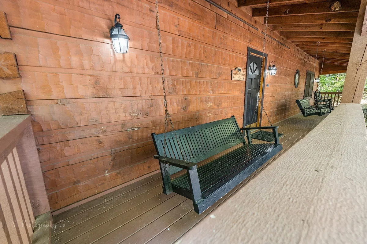 This image shows a welcoming exterior porch with wooden swings, the front door, and charming wall lanterns. The porch is set against a backdrop of trees, offering a tranquil and inviting outdoor space ideal for relaxation and quiet moments together.
