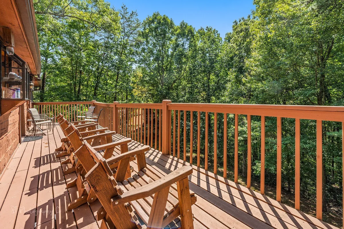A spacious wooden deck with classic Adirondack chairs nestled among lush greenery. The environment is peaceful with trees surrounding the deck, inviting guests to relax, socialize, or take in the natural beauty. The open setting suggests opportunities for both daytime lounging and evening stargazing.