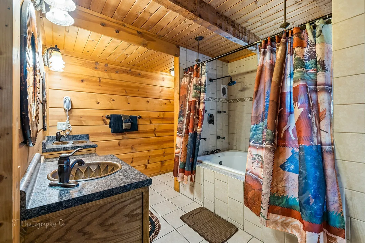 A warm, inviting bathroom with wooden walls, a decorative shower curtain, double sinks, and a bathtub. The space exudes tranquility and comfort, ideal for both shared and private routines.