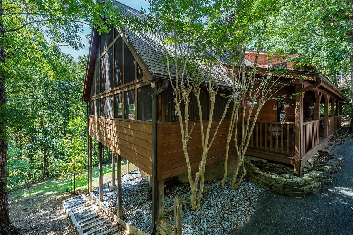 This image captures the exterior of Smoky Mountain Lodge, highlighting a rustic wooden structure with a screened porch nestled among trees and set beside a stone path. The tranquil outdoor setting speaks to the lodge’s natural surroundings and welcoming entrance.