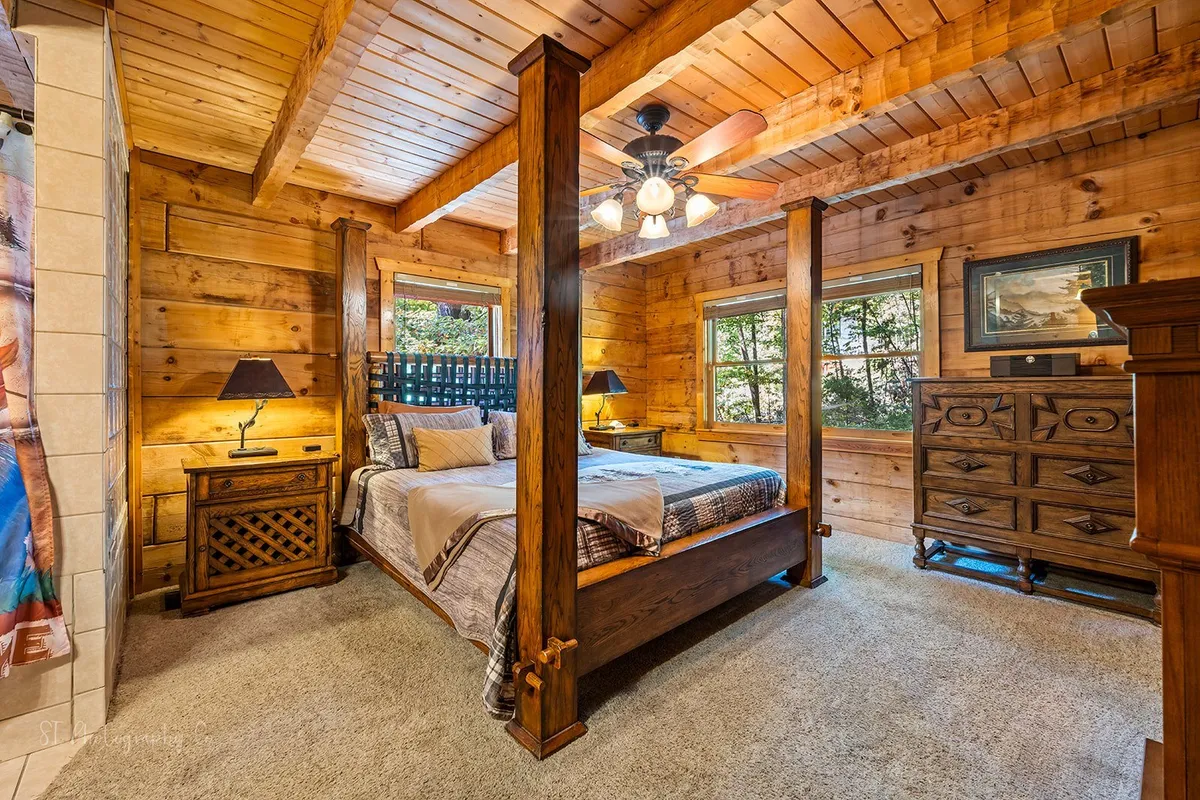 A tranquil bedroom featuring a four-poster bed, wooden dresser, large windows with ample natural light, and bedside lamps. The room exudes comfort and peace, perfect for unwinding after a busy day.