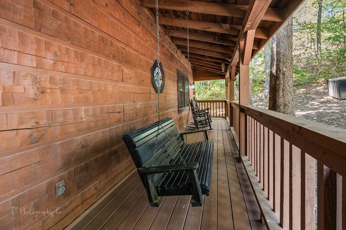 This image shows a peaceful wooden porch adorned with swing chairs, surrounded by lush natural greenery. The view from the porch looks out onto the woods, immersing the seating area in the tranquility of the Smokies. The design invites guests to relax and savor the gentle mountain breezes.