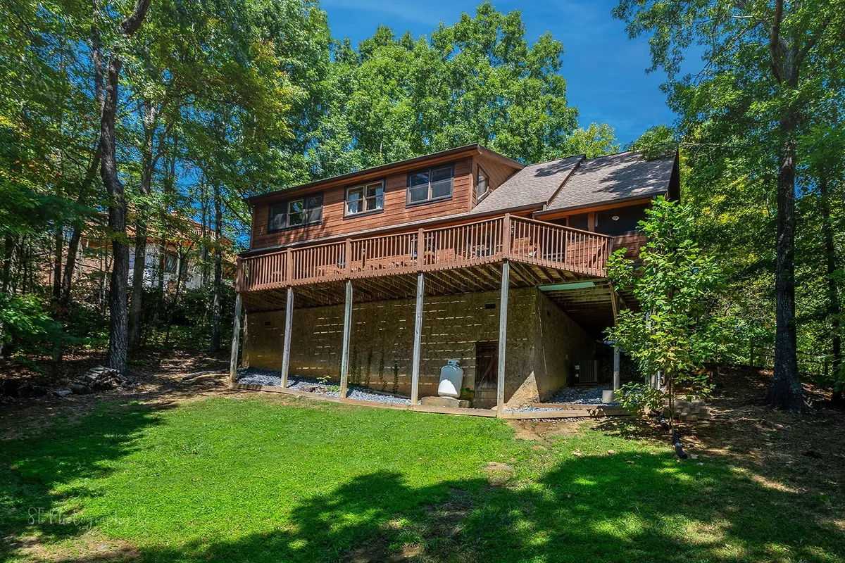 The photo captures an elevated wooden deck overlooking a lush green lawn and surrounded by trees. The setting is peaceful and ideal for outdoor family gatherings or simply relaxing after a day exploring the Smoky Mountains.
