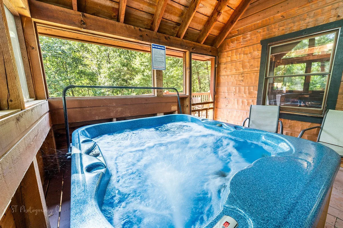 A cozy interior with a private hot tub nestled by wooden beams and open windows, allowing natural light to stream in. The hot tub area is designed for relaxation, privacy, and intimate moments while soaking and enjoying the surrounding nature.