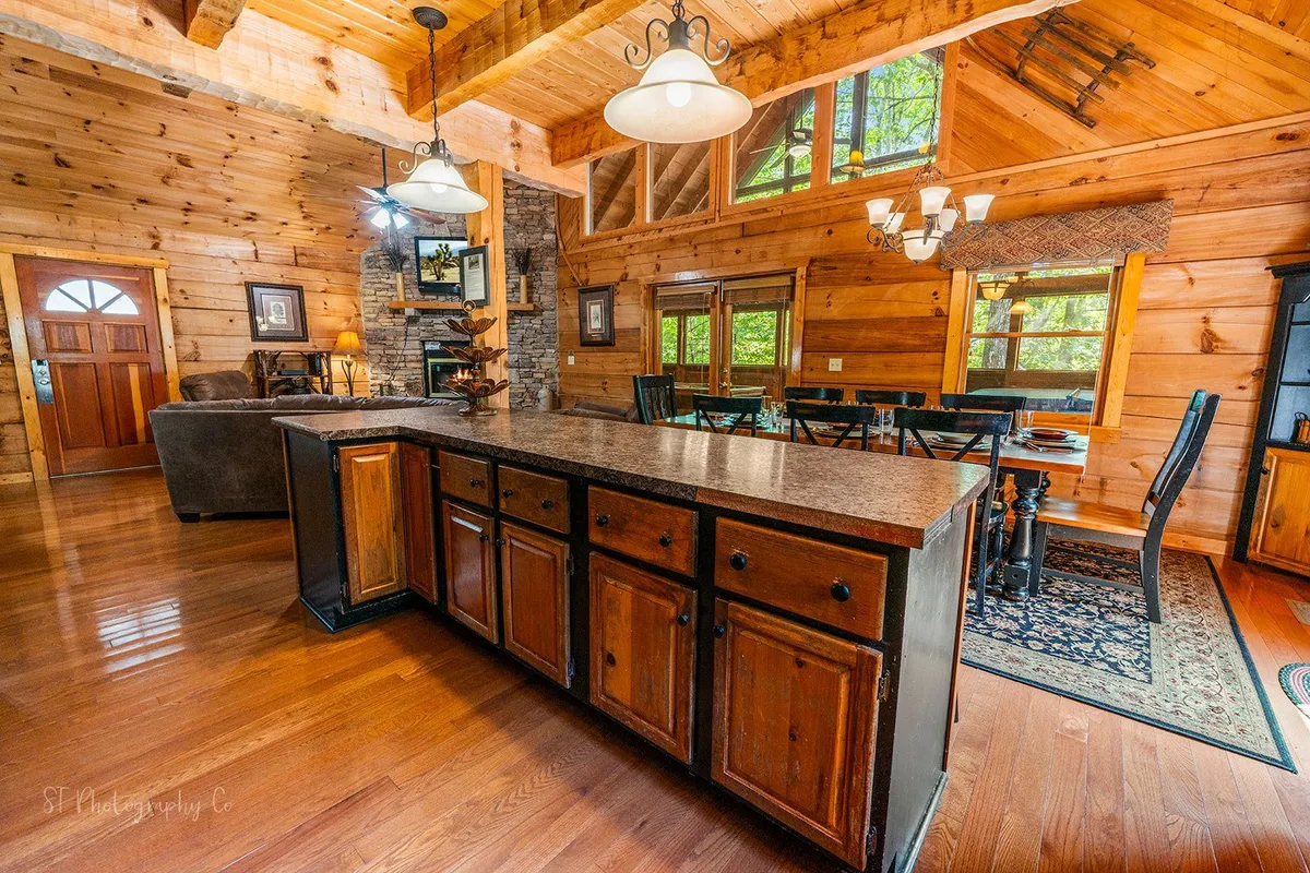This image provides a wide view of the open-concept communal area, seamlessly blending the kitchen, dining area, and living room with a fireplace, wooden beams, and large windows. The design encourages easy movement and interaction among guests.